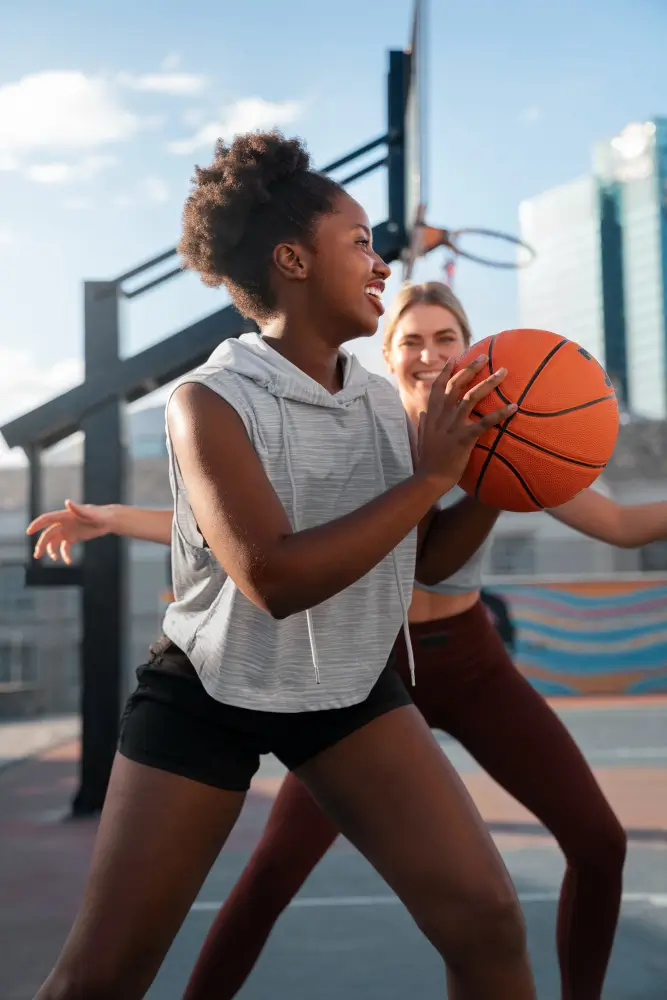 Young woman holds basketball while smiling on an outdoor city court.